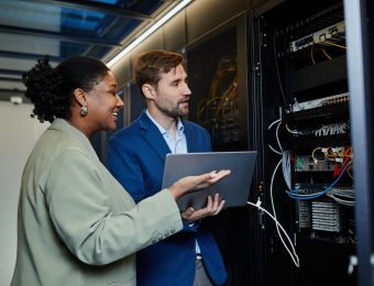 Portrait of two people in server room using laptop and setting up data security network